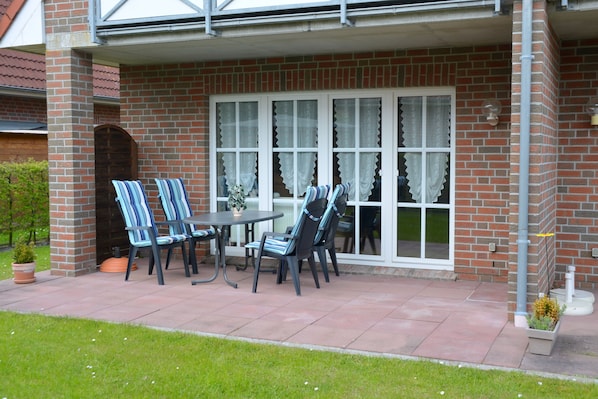 A patio with a brick wall, a covered seating area with striped chairs and a table, and a large window with curtains.