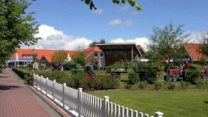 Een geplaveid pad langs een witte hekken, leidend naar een gebouw met een rood dak.