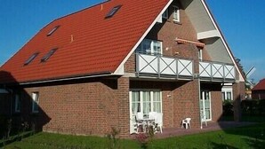 Een tweelaags huis met een rood dak, een balkon en een gevel van baksteen.