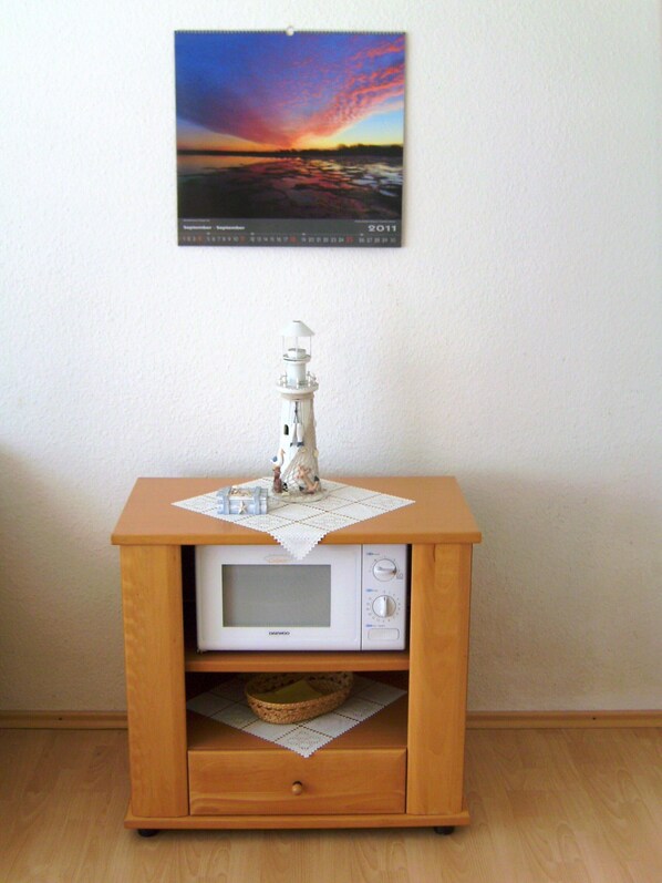 A wooden cabinet with a microwave, a small basket, and a decorative lighthouse model on top.