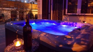Un bain à remous avec une bouteille et une bougie sur une table, entouré d’un mur de pierre et d’une fenêtre.