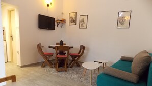 Un salon avec un canapé de couleur turquoise, des chaises en bois, une petite table, un téléviseur fixé au mur et des œuvres d’art encadrées.