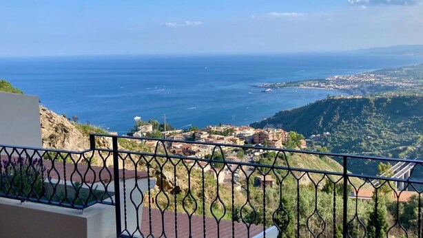 Vista costera desde un balcón con barandilla metálica, que da a un pueblo y al mar.