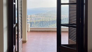 Una puerta abierta que da a un balcón con vistas a montañas lejanas y una barandilla.