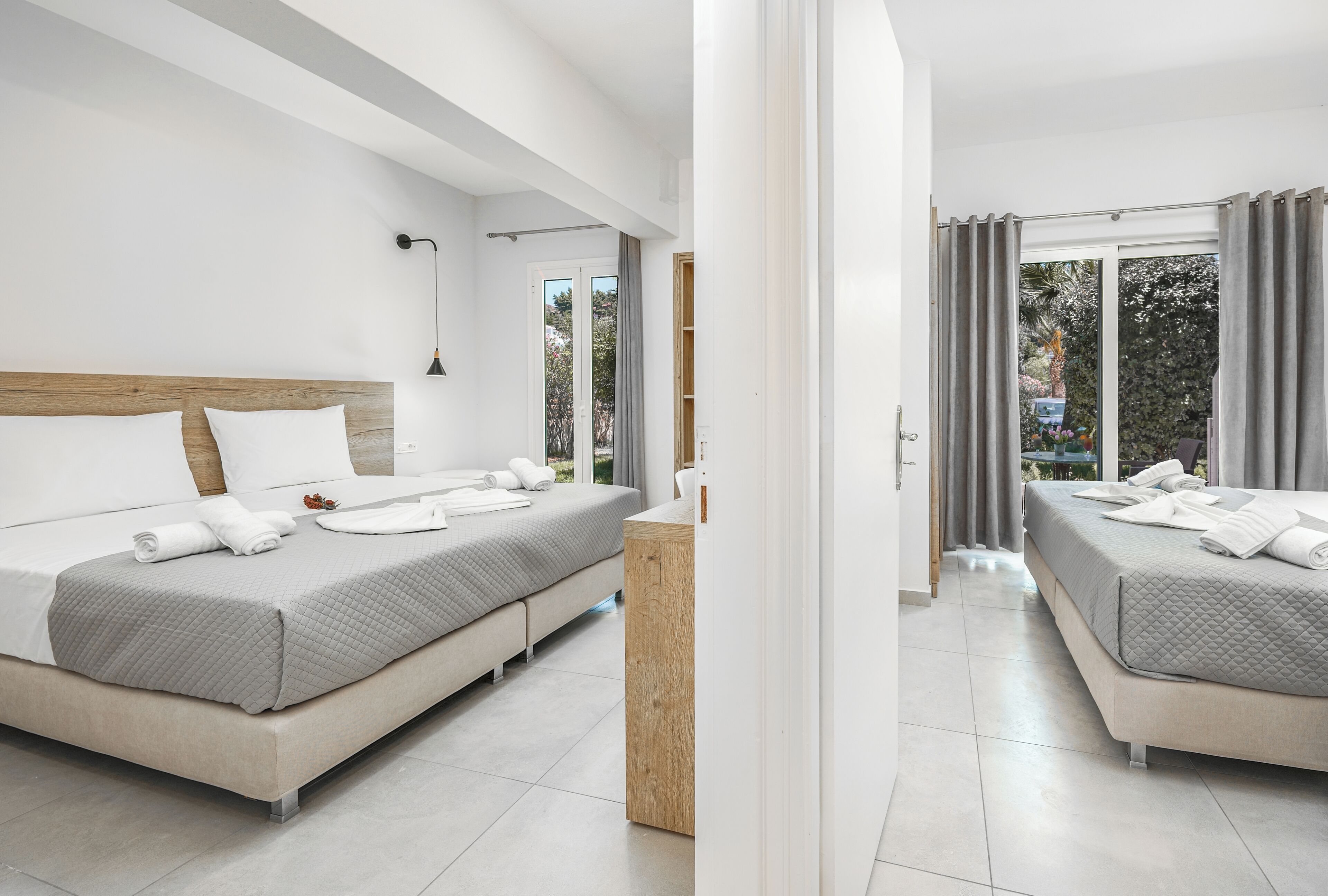 A modern hotel room with two beds, a wooden headboard, a bedside table, and a view of the outdoors.