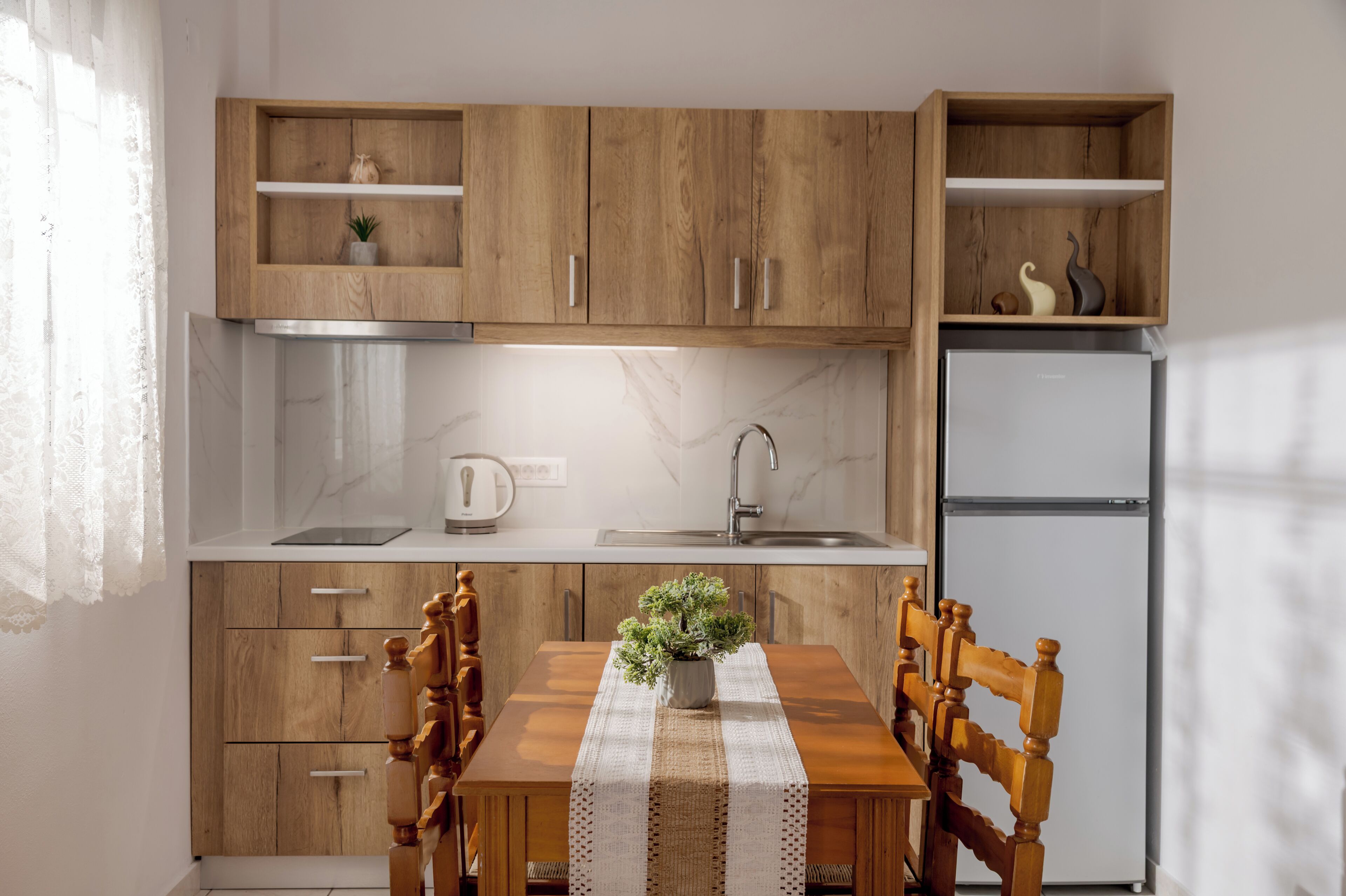 A kitchen with wooden cabinets, a marble countertop, a sink, a refrigerator, and a dining table with chairs.