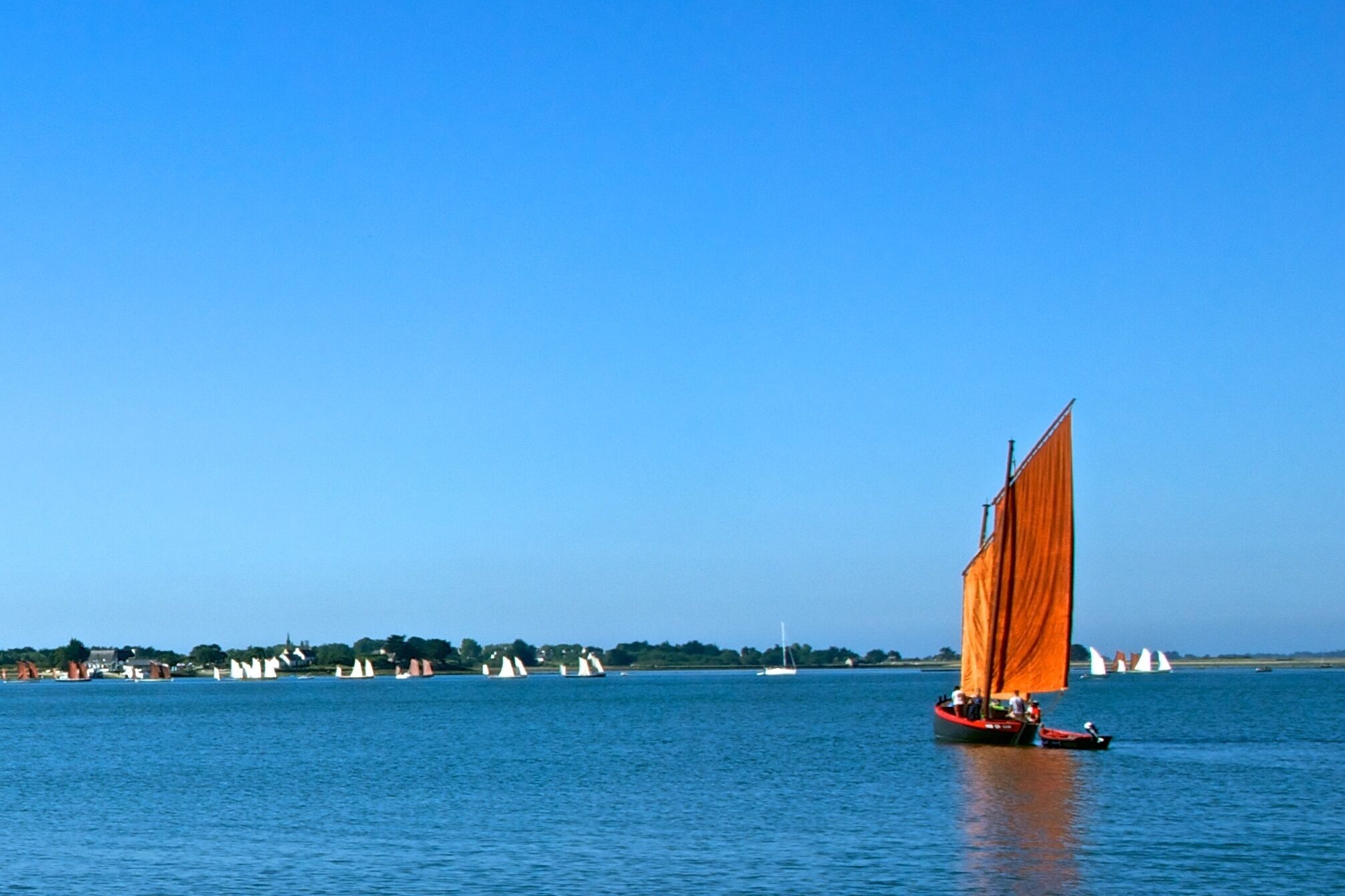 Un voilier à la voile orange sur une étendue d’eau calme.