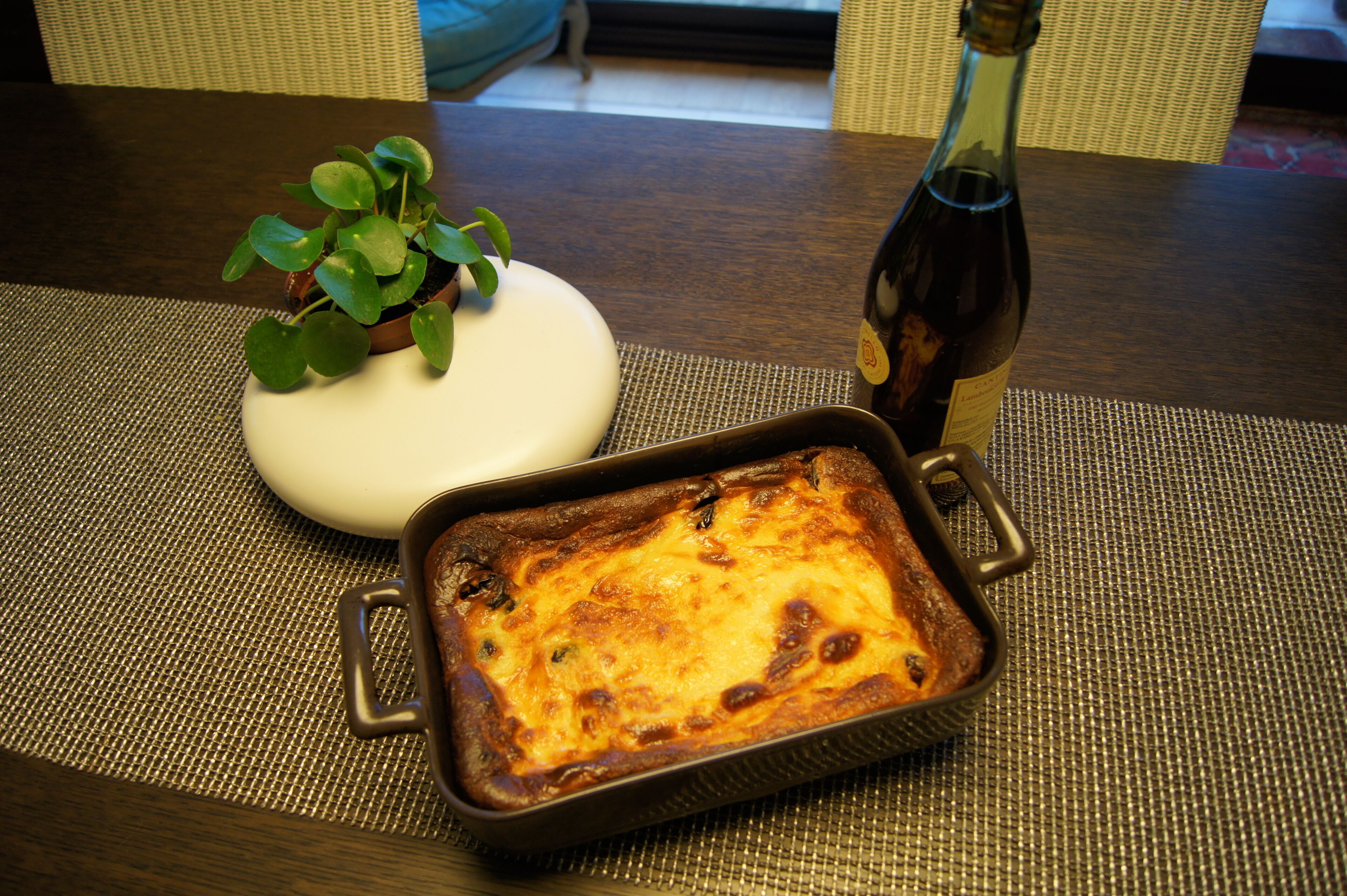 A rectangular baking dish with a golden-brown baked dish on a woven placemat.