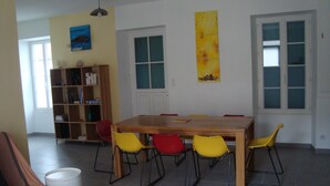 A dining area with a wooden table and six chairs, a bookshelf, and a window with blinds. - House close to all shops (Saint-Denis-d'Oléron)