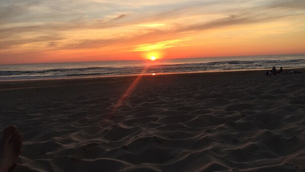 Ein Strand bei Sonnenuntergang, die Sonne geht über dem Meer unter.