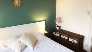 Ein Schlafzimmer mit einem Bett, Kissen, einem Nachttisch, einer Lampe, einer Holzkommode und einer Orchidee im Topf.