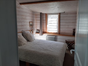 A bedroom with a bed, a window with curtains, a bedside table, and a small shelf.