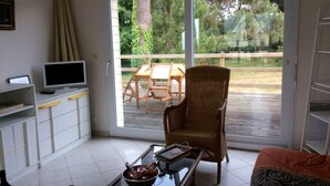 A room with a television on a cabinet, a wicker chair, a glass table with a bowl, and a sofa.
