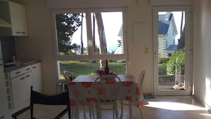 A dining area with a table set for four, a black folding chair, and a view of the outdoors through a glass door.