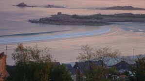 A coastal landscape with a curved shoreline, rocky outcrops, and residential buildings in the foreground.