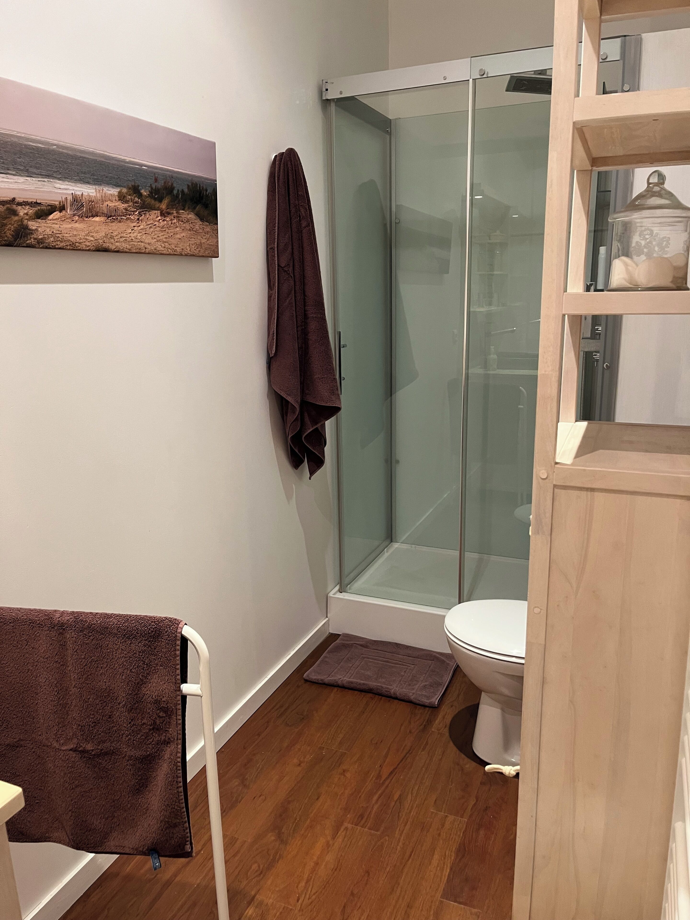 A bathroom with a glass shower enclosure, a toilet, and a wooden cabinet.
