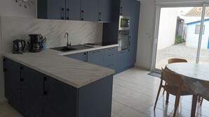 Una cocina moderna con armarios azul oscuro, una encimera de mármol blanco y un horno empotrado. Se ve un área de comedor con una mesa y sillas a través de una puerta de cristal.