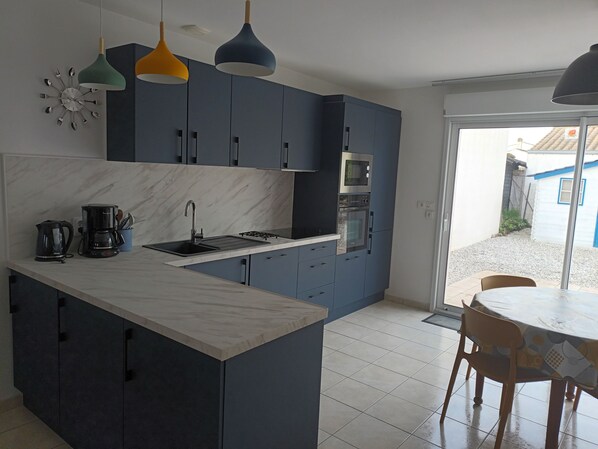 Eine moderne Küche mit dunkelblauen Schränken, einer weißen Marmorarbeitsplatte und einem eingebauten Backofen. Durch eine Glastür ist ein Essbereich mit Tisch und Stühlen zu sehen.