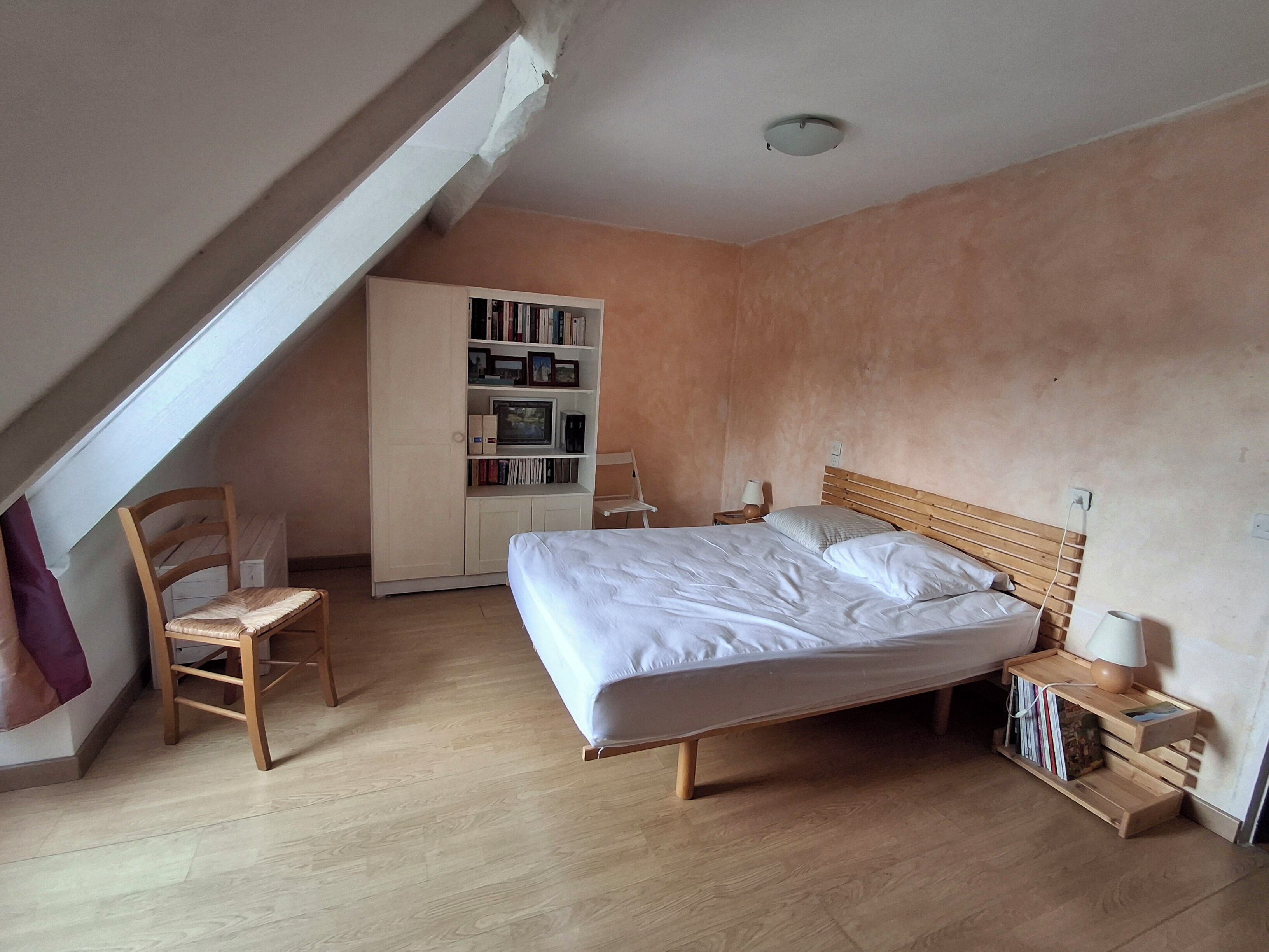 A bedroom with a wooden bed, a bookshelf, a chair, and a desk with a lamp.