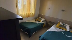 A room with two single beds, a desk, and a hanging light fixture.