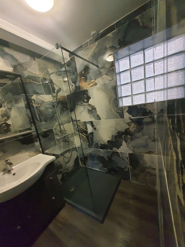 A bathroom with a glass shower enclosure, a sink, and a mirror.