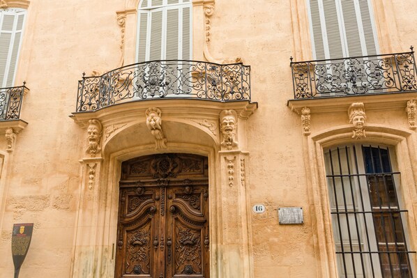 A building facade with ornate iron balconies, a large wooden door with intricate carvings, and a plaque with a number.