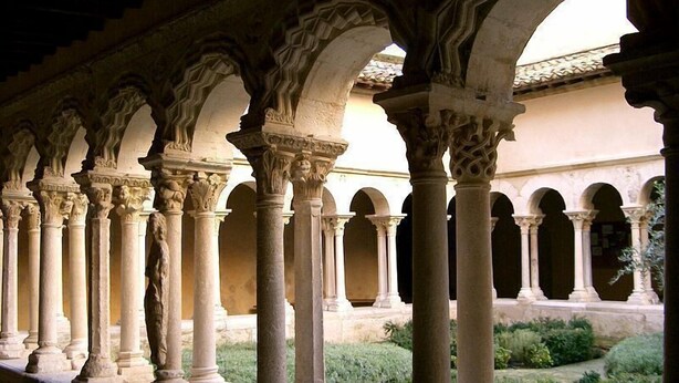 Una serie de arcos sostenidos por columnas en un patio con vegetación.