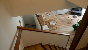 Un interior moderno con una escalera de madera, una zona de comedor con mesa y sillas, un sofá y una planta en maceta.