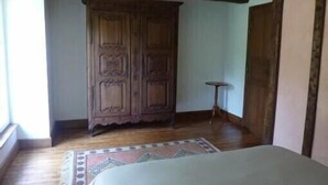 Une pièce comprenant une armoire en bois, une petite table ronde et un lit recouvert d’une couvre-lit à motifs.