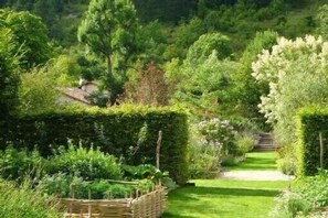 Ein Gartenweg mit ordentlich geschnittenen Hecken und einem Korbwägelchen.