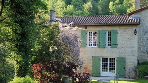 Une maison en pierre avec des volets verts, un toit de tuiles et un jardin agrémenté d’une table et de chaises.