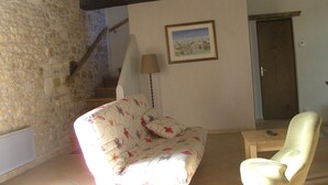 Ein Zimmer mit Steinsandsteinwand, einer Holztreppe, einem Sofa, einem Sessel und einem gerahmten Bild an der Wand.