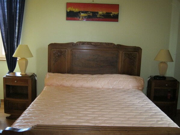 A neatly made bed with a quilted headboard, two bedside tables with lamps, and a painting on the wall.