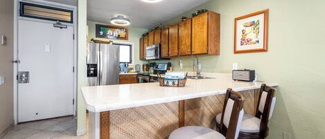 A kitchen with a central island, wooden cabinets, a microwave, and a refrigerator.