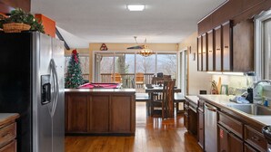 Une cuisine spacieuse dotée de meubles en bois, d’un réfrigérateur en acier inoxydable et d’un coin repas agrémenté d’un sapin de Noël.