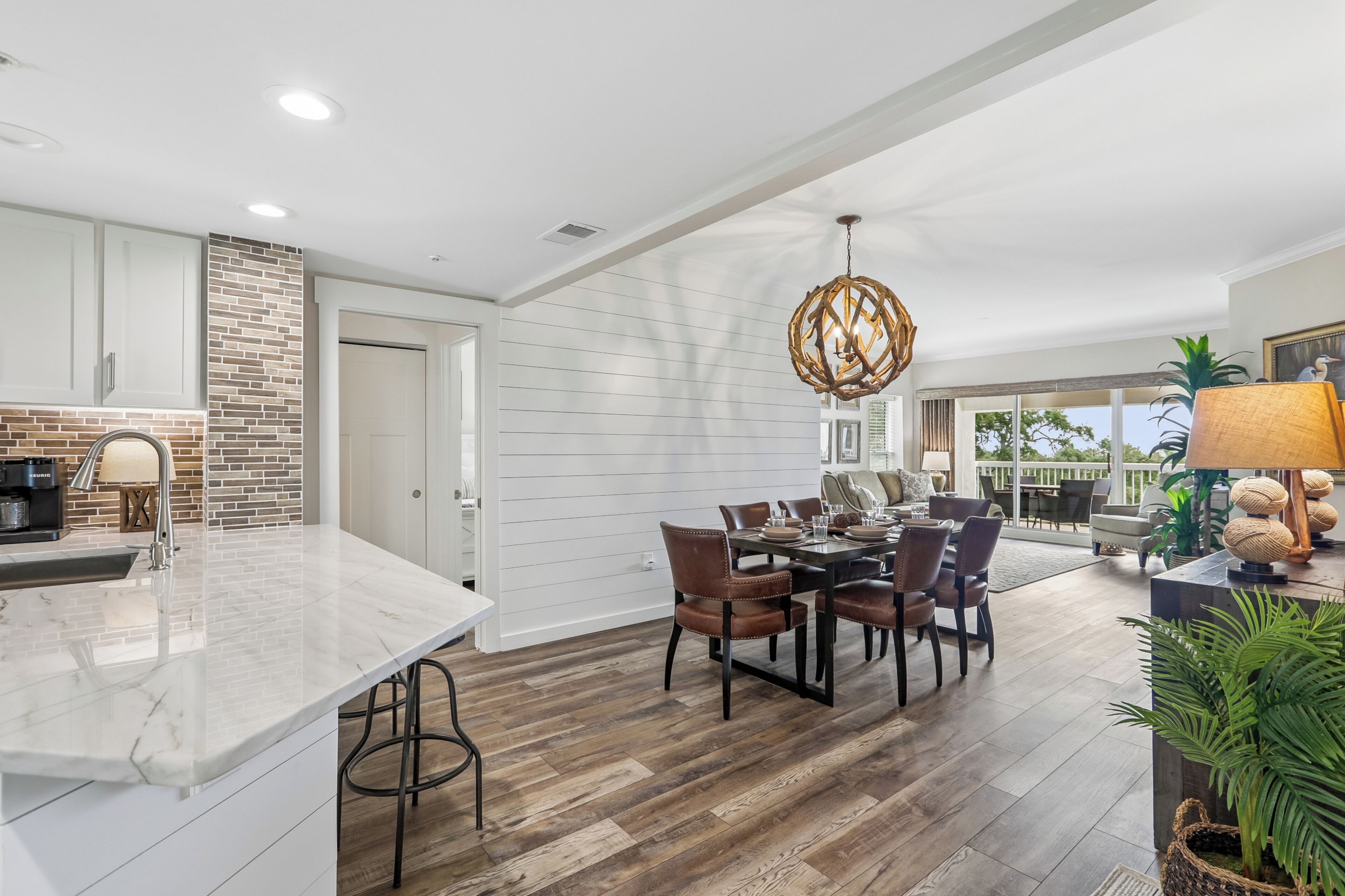 A spacious kitchen with a marble countertop, a dining area with a wooden table and chairs, and a large window offering a view of the outdoors.