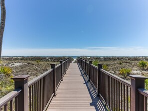A wooden boardwalk leading to a beach with a clear sky.