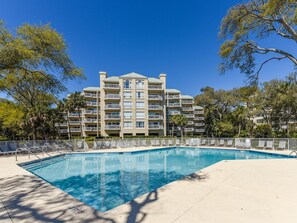 A hotel with a swimming pool, multiple balconies, and surrounding trees.
