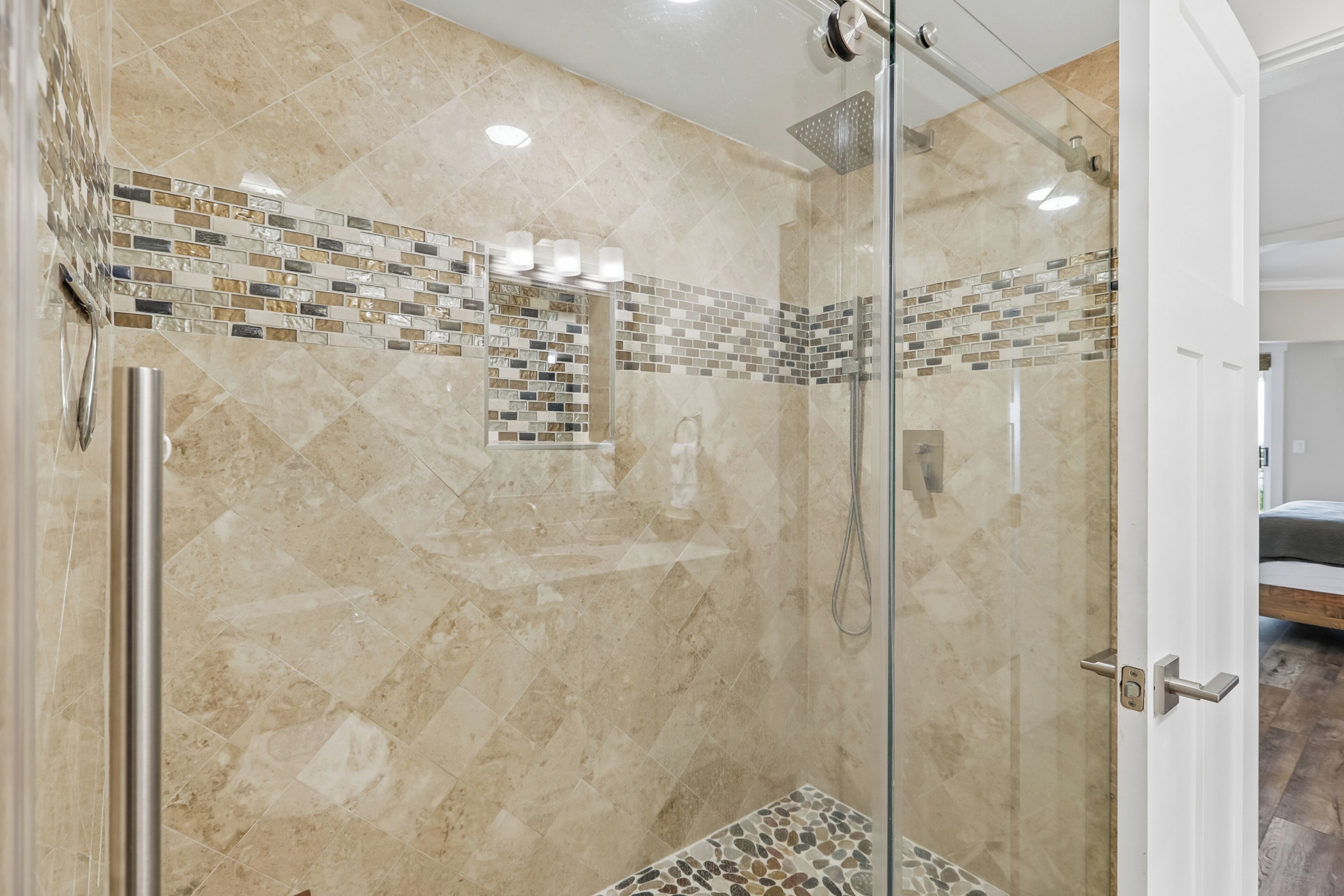A modern shower with a glass door, a tiled mosaic backsplash, and a handheld showerhead.