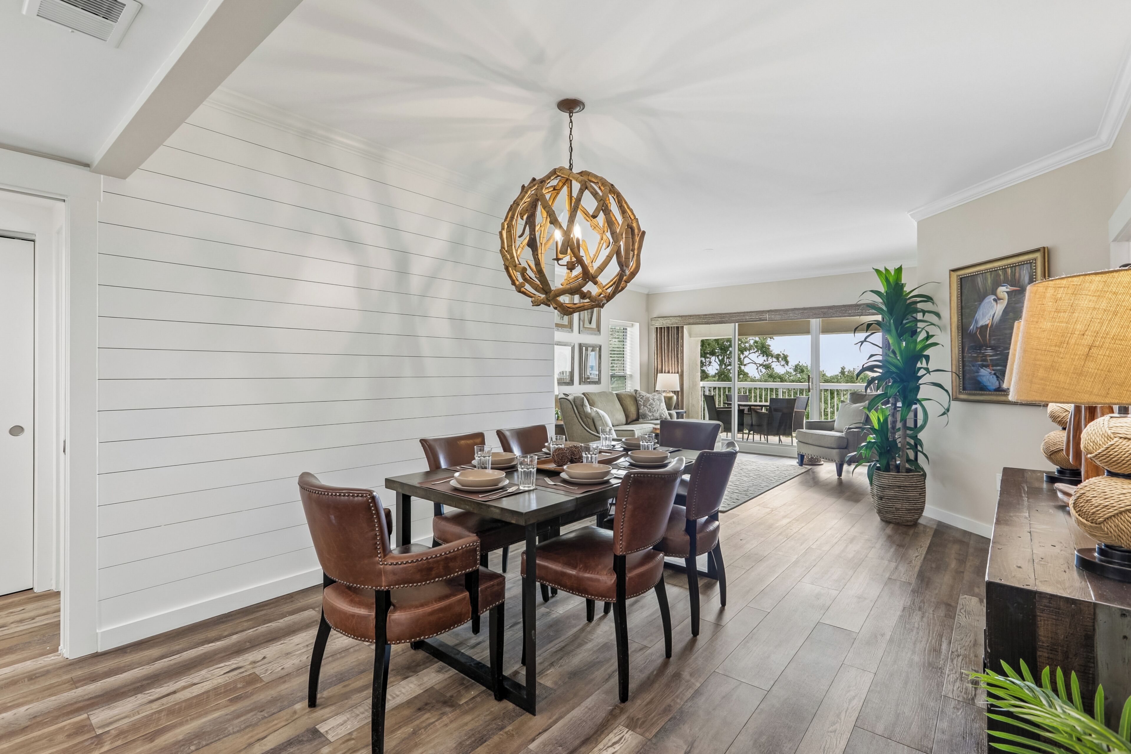 A dining area with a wooden table and chairs, a hanging light fixture, and a view of the outdoors.