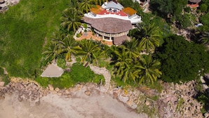 An aerial view of a resort with a central building surrounded by palm trees, a beach, and rocky terrain. - Secluded Beachfront Sanctuary w/ Epic Sunsets & Palapa Lounge (Higuera Blanca)