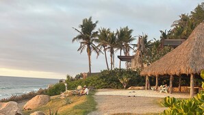 A pathway leading to a beach area with palm trees and a thatched-roof structure. - Secluded Beachfront Sanctuary w/ Epic Sunsets & Palapa Lounge (Higuera Blanca)