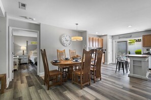 A modern kitchen with wooden cabinets, a dining area with a round table and chairs, and a visible clock on the wall. - Stunning Beach Home/Private pool with large backyard/ 7 Min walk to beach (Hilton Head Island)