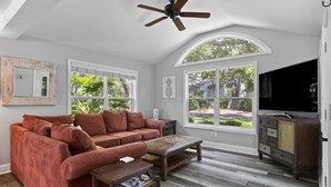 Un salon spacieux doté d’une grande fenêtre, d’un ventilateur de plafond, d’un banc en bois et d’un téléviseur.