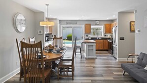 Une cuisine moderne avec des meubles en bois, un coin repas avec une table et des chaises en bois, et un canapé gris dans un salon spacieux.