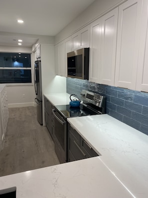 Una cocina moderna con armarios blancos, un refrigerador de acero inoxidable, un microondas y una estufa.