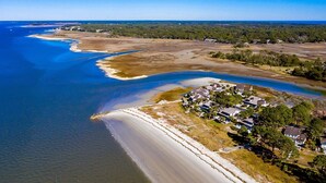 An aerial view of a coastal area with a beach, a residential area with houses, and a clear blue sky. - Enjoy the Amazing Views from this Beach Cottage (Hilton Head Island)
