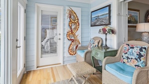 A room with a light blue wall, a door with a decorative spiral, wicker furniture, and a framed picture on the wall. - Enjoy the Amazing Views from this Beach Cottage (Hilton Head Island)
