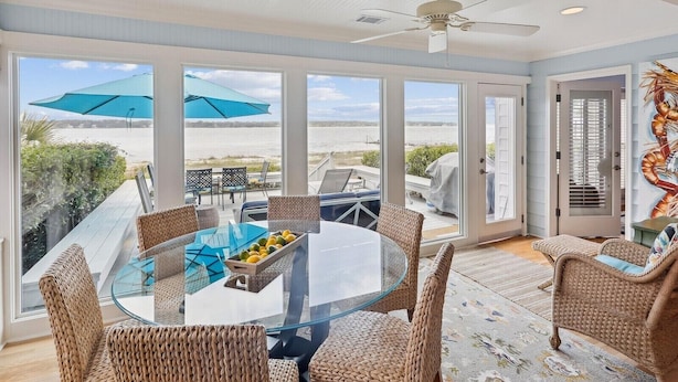 A sunlit room with a glass table, wicker chairs, and a view of the beach. - Enjoy the Amazing Views from this Beach Cottage (Hilton Head Island)