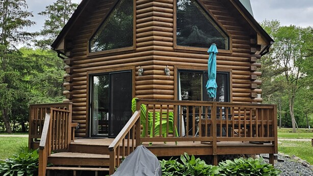 Una cabaña de madera con un porche de madera, un área de estar cubierta al aire libre y un gran ventanal.
